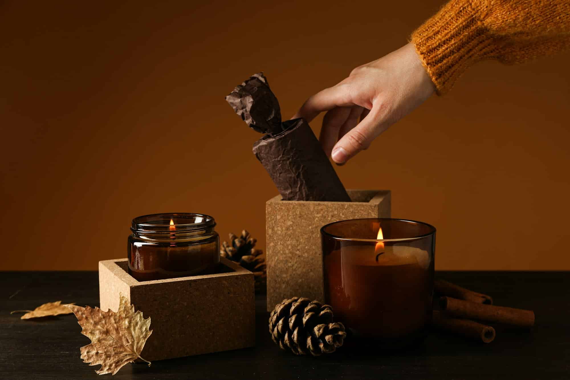 Candles, cones and female hand on brown background