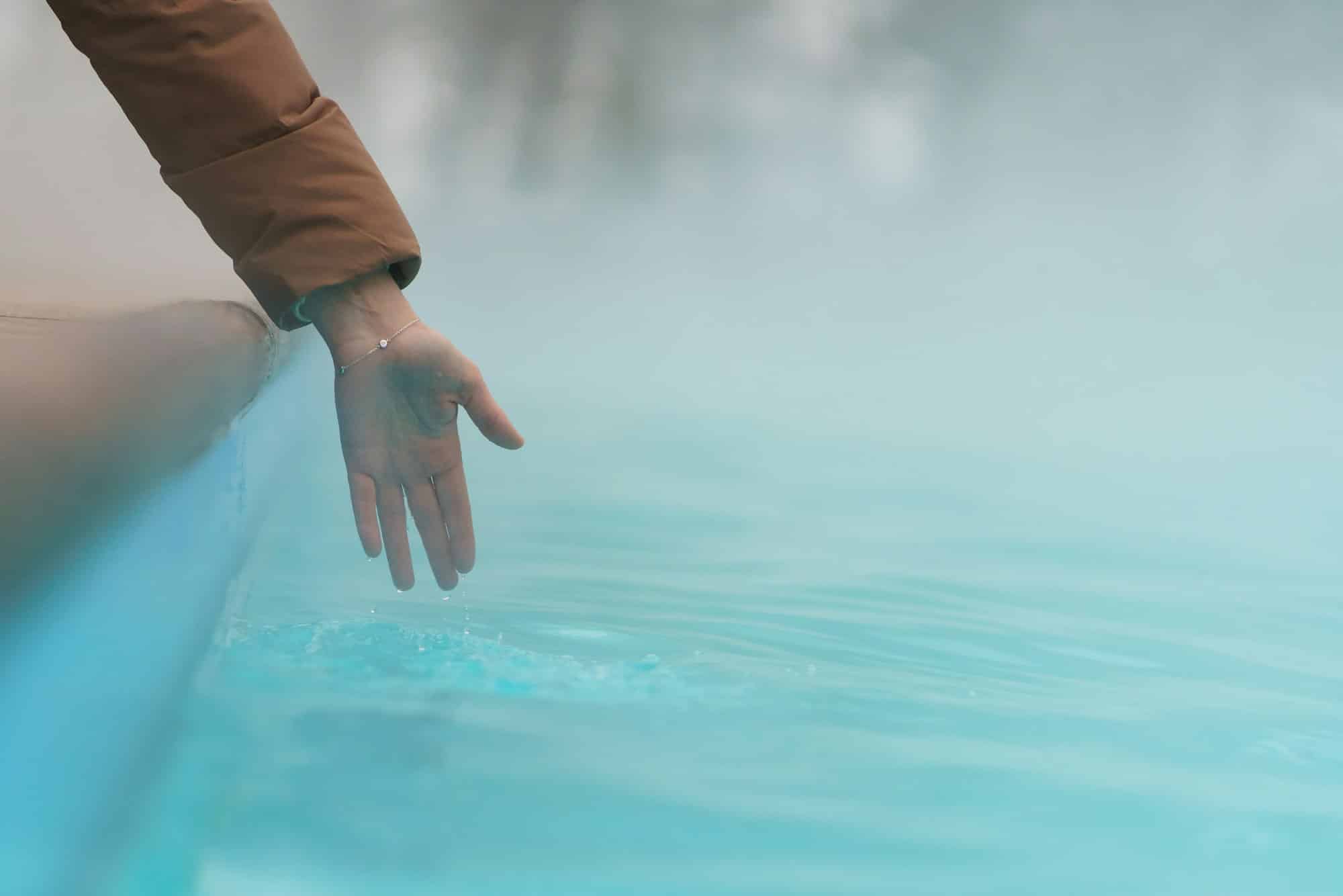 Hand of woman checking temperature of water in open swimming pool in winter. Thermal spa outdoor.