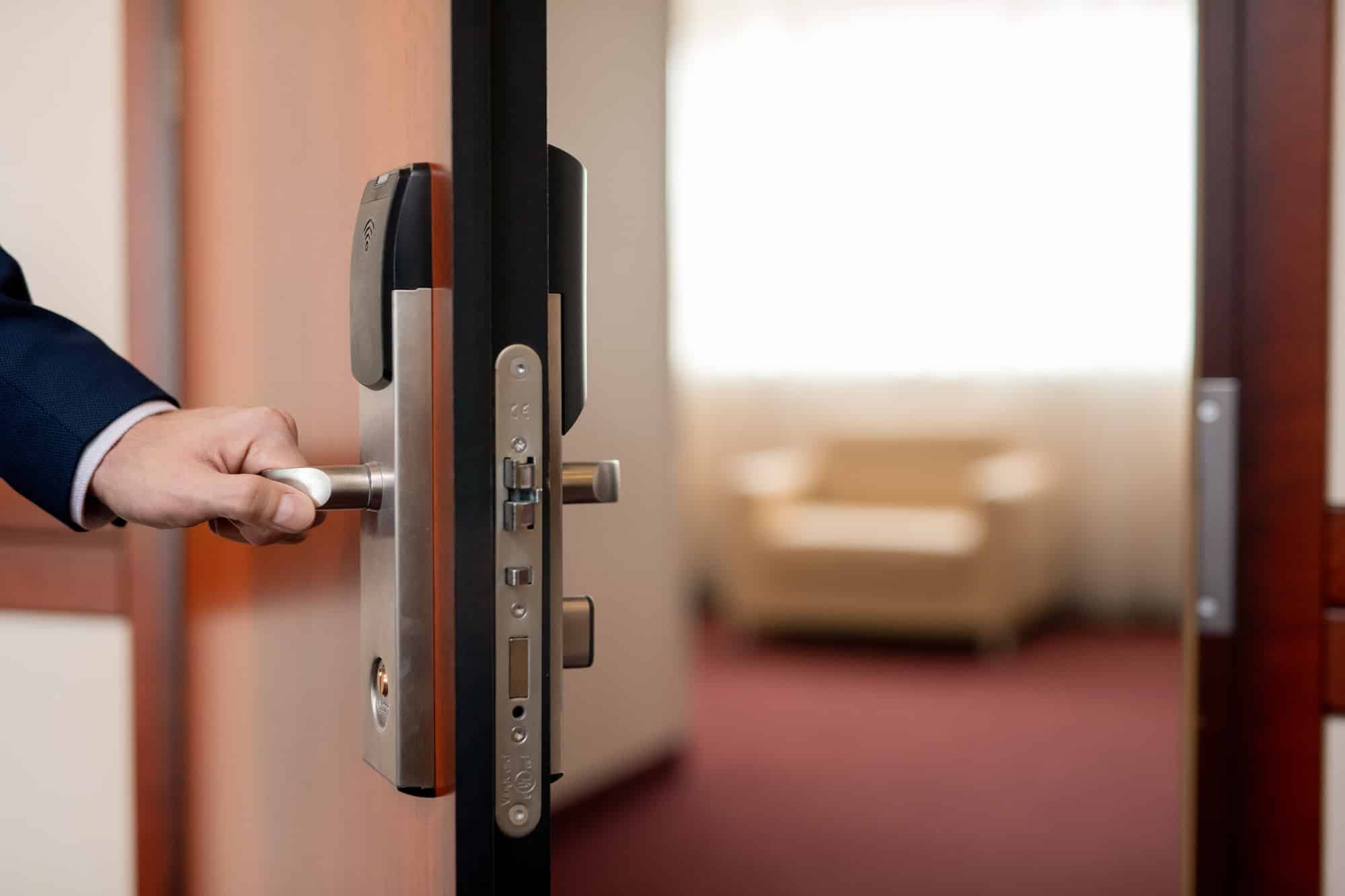 Human hand holding handle of wooden door while entering one of hotel room